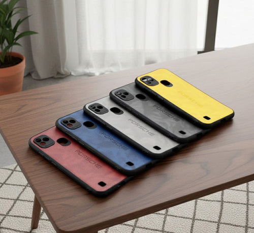 Five Porsche-branded phone cases in red, blue, gray, black, and yellow are arranged diagonally on a wooden table in a bright room.